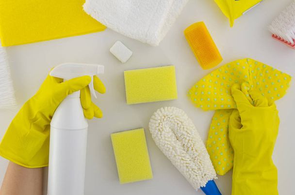 Woman hands in ruber gloves holds spray and rag. Cleaning service concept. Yellow cleaning set for different surfaces in kitchen, bathroom and other rooms. . Top view on white background - Photo, Image
