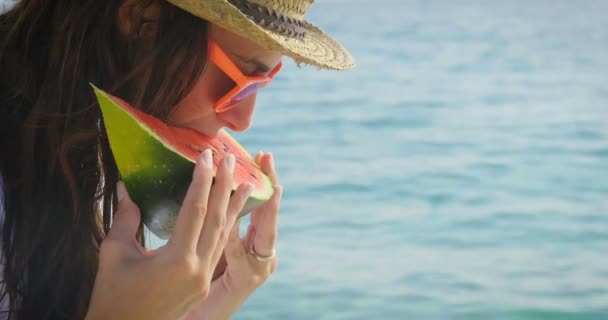 video of woman in hat and sunglasses eating fresh sweet watermelon slice at blue sea  - Video, Çekim