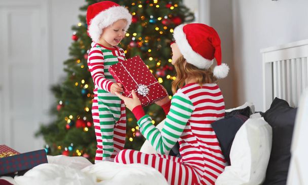 feliz familia madre abrazo su bebé hijo en pijama apertura regalos en la mañana de Navidad cerca de Navidad tre
 - Foto, Imagen