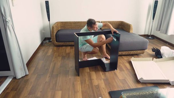 Un giovane colleziona mobili in modo indipendente nel soggiorno della sua casa. Un uomo raccoglie una scrivania del computer
. - Foto, immagini