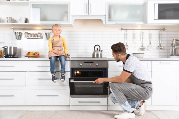 Young man and his son baking something in oven at home - Foto, imagen