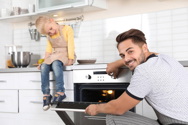 Young man and his son baking something in oven at home - Foto, Bild