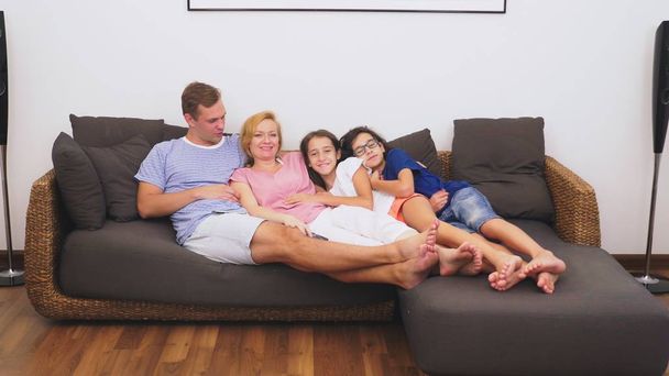 Viehättävä perhe, äiti, isä, tytär ja poika katsovat televisiota olohuoneessa yhdessä.
 - Valokuva, kuva