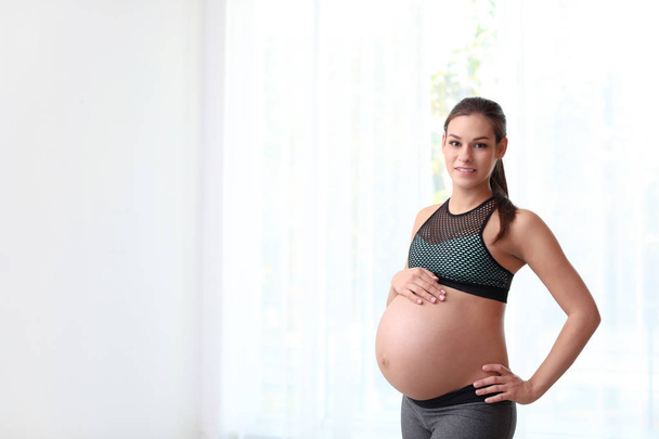 Young pregnant woman in fitness clothes at home. Space for text - Φωτογραφία, εικόνα