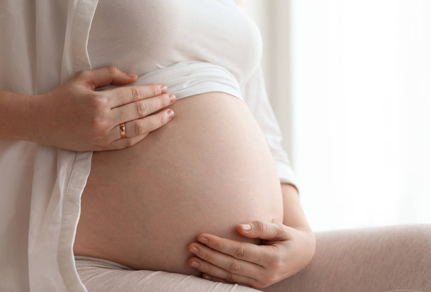Pregnant woman sitting in light room at home, closeup - Fotografie, Obrázek