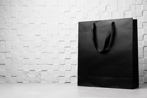 Paper shopping bag with ribbon handles on table near white wall. Mockup for design - Foto, afbeelding