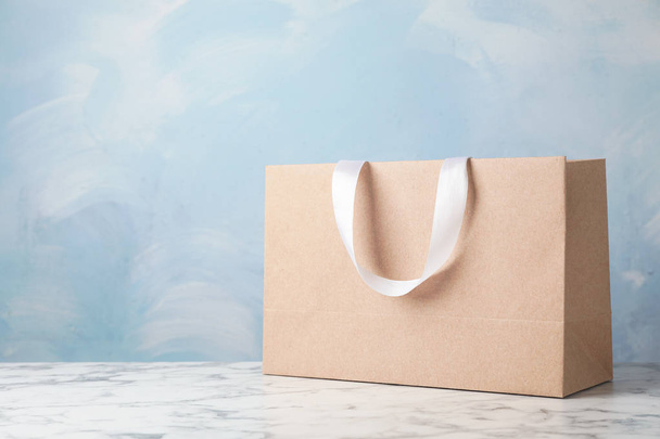 Paper shopping bag with ribbon handles on table against color background. Mockup for design - Φωτογραφία, εικόνα