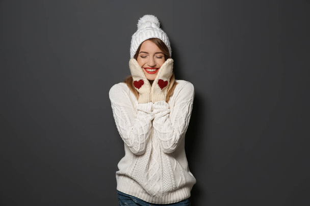 Beautiful young woman in warm sweater with hat and mittens on dark background - 写真・画像
