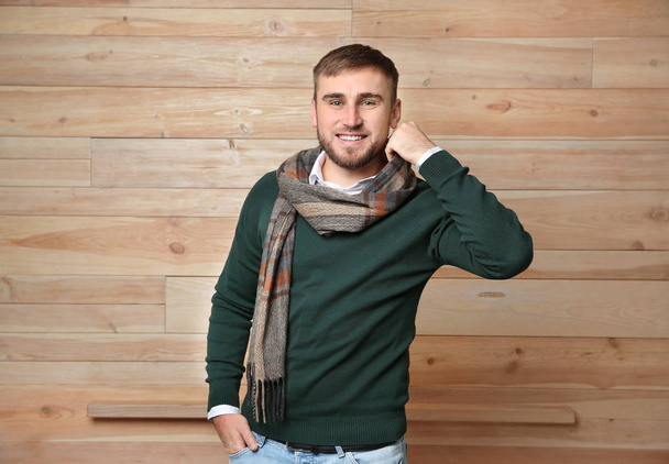 Handsome young man in warm sweater with scarf on wooden background - Photo, Image