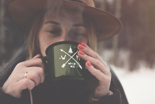 Girl drinking hot tea outdoors from a green mug in the winter day  - Fotó, kép
