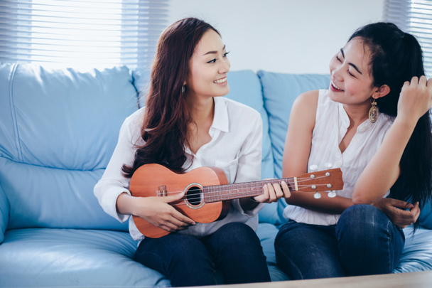 Two asia women are having fun playing ukulele and smiling at home for relax time - Photo, Image