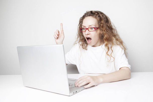 εκφραστική Κοκκινομάλλης γυναίκα με δημιουργική ιδέα λειτουργεί με laptop μπροστά από το λευκό τοίχο και δείχνει προς τα επάνω - Φωτογραφία, εικόνα