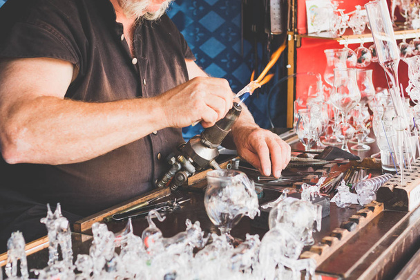 Die Hände des Kunsthandwerkers, der auf dem Kunsthandwerkermarkt ein Glasobjekt herstellt. Glasbläsermeister arbeitet im Park - Foto, Bild