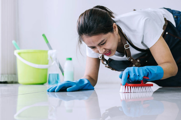 Housekeeping and cleaning concept, Happy young woman in blue rubber gloves wiping dust using a spray and a brush while cleaning on floor at home. - Photo, image