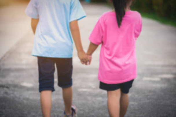 Vervagen de achtergrond van rug weergave jongere Aziatische broertjes en zusjes hand in hand lopen. liefde familie concepten - Foto, afbeelding