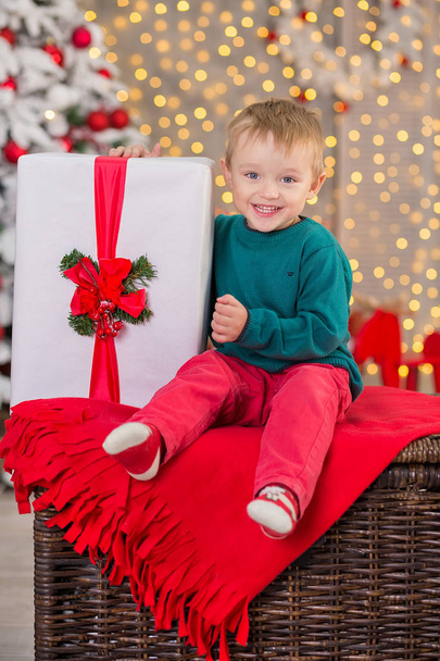 Christmas family child boy posing on wooden box close to presents and white fancy new year tree wearing red and green clothes - 写真・画像
