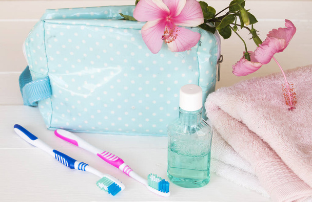 Frottee, Mundwasser, Zahnbürste Gesundheitsversorgung für die Mundhöhle in blauer Tasche Reise mit rosa Blumen Hibiskus auf weißem Holz Hintergrund - Foto, Bild