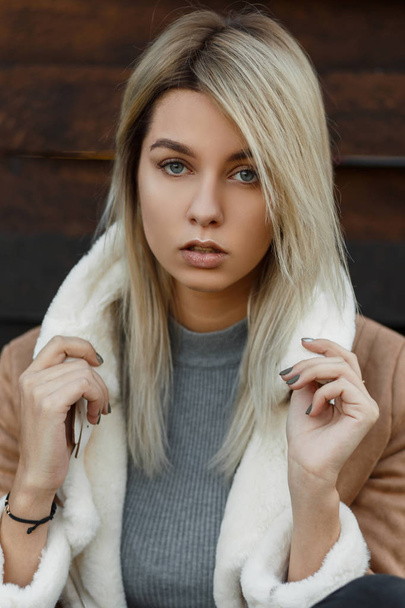 Portret van een saucy blond meisje met blauwe ogen, natuurlijke make-up in een modieuze herfst-voorjaar jas, kijkt in de camera met een ernstige of doordachte uitdrukking op haar gezicht. Aantrekkelijke vrouw. - Foto, afbeelding