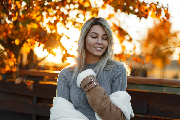 Uroczy szczęśliwy młoda kobieta w sezonowe ubrania pozowanie i uśmiecha się na tle Złotego drzewa, piękny jasny pomarańczowy zachód słońca. Atrakcyjna dziewczyna w ciepły, jesienny dzień słoneczny. - Zdjęcie, obraz