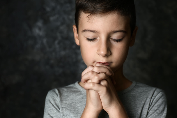Pieni poika rukoilee tummalla taustalla
 - Valokuva, kuva