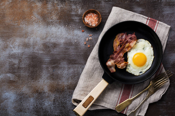 Traditional English breakfast with fried eggs and bacon in cast iron pan on dark concrete background. Top view. - Valokuva, kuva