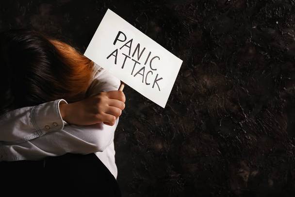 Depressed woman holding paper with text PANIC ATTACK on grey grunge background - Photo, Image