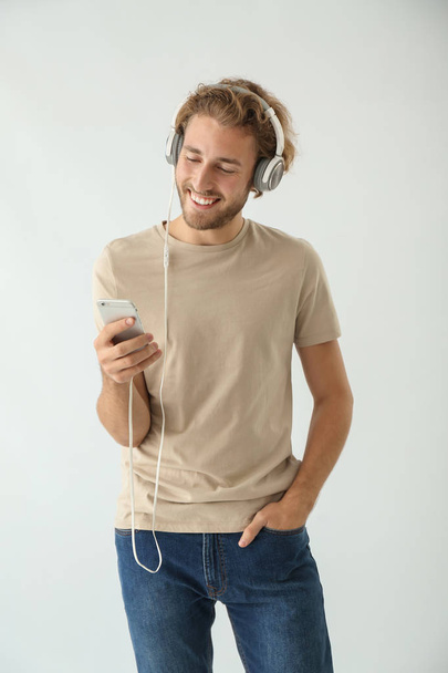 Handsome man listening to music on light background - Фото, зображення