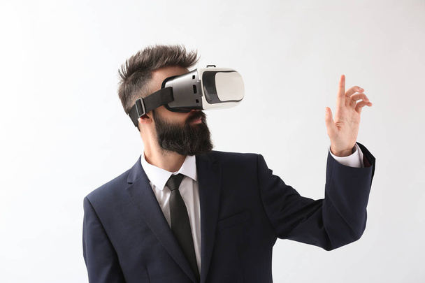 Businessman wearing virtual reality glasses on light background - Foto, afbeelding