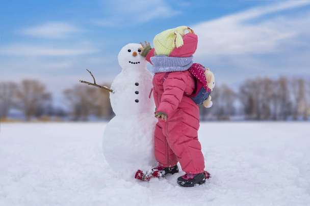 Cute child girl making snowman at bright snowy place. Winter outdoor activities - Фото, изображение