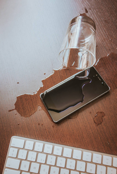 Смартфон и клавиатура случайно промокли на деревянном столе. Glass o
 - Фото, изображение