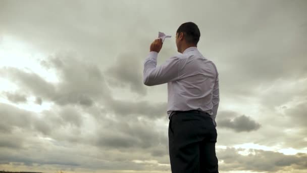 Businessman in white shirt is playing with paper flying airplane against background of dark clouds. Slow motion - Footage, Video