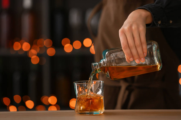 Θηλυκό μπάρμαν ρίχνει ουίσκι από το μπουκάλι στο ποτήρι στο τραπέζι - Φωτογραφία, εικόνα