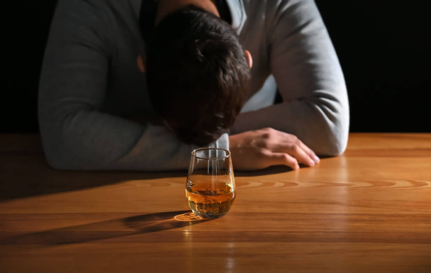 Unconscious drunk man with glass of whiskey at table - Фото, зображення