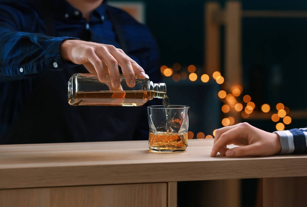 Чоловік бармен поливає віскі з пляшки в склянку в барі
 - Фото, зображення