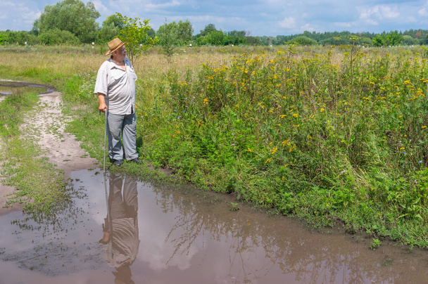 Ανώτερος άνθρωπος στέκεται κοντά μεγάλη λακκούβα στο δρόμο χώρας - Φωτογραφία, εικόνα
