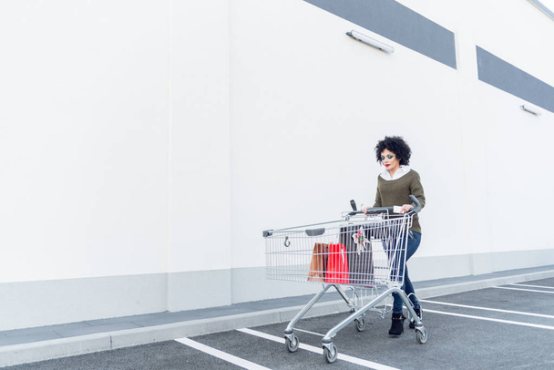 young beautiful woman pushing shopping cart with bags  - Fotoğraf, Görsel