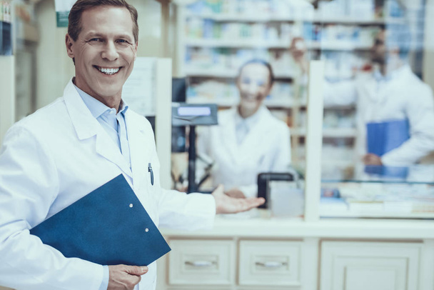 Pharmacists is Working. Adult Male Pharmacist Showing a Counter of Pharmacy. Two Young Pharmacists Working on Counter. People Wearing a Special Medical Uniform. People Located in Pharmacy. - Photo, image