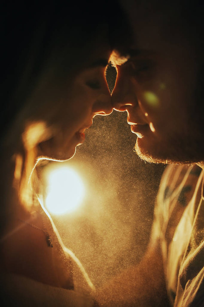 Retrato de la joven pareja enamorada de pie cara a cara contra la luz de la lámpara con retroiluminación
. - Foto, Imagen