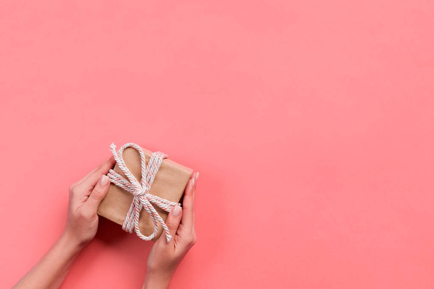 Woman arms holding gift box with pink ribbon on color background, top view. - Photo, Image