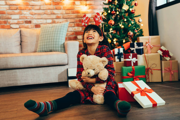 Sweet little girl hugging teddy bear looking up to sky smiling sitting on wooden floor. attractive childhood received gift on Christmas sale at home. kid with reindeer satisfied with present. - Foto, immagini
