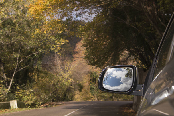 Έννοια του ταξιδιού. Όμορφο ουρανό και τα σύννεφα στο sideview αυτοκίνητο καθρέφτη σε ορεινό δρόμο - Φωτογραφία, εικόνα