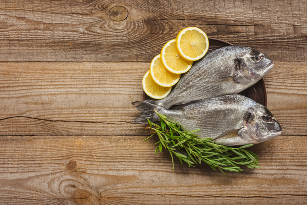 top view of raw fish with lemon and rosemary on wooden table - Photo, image