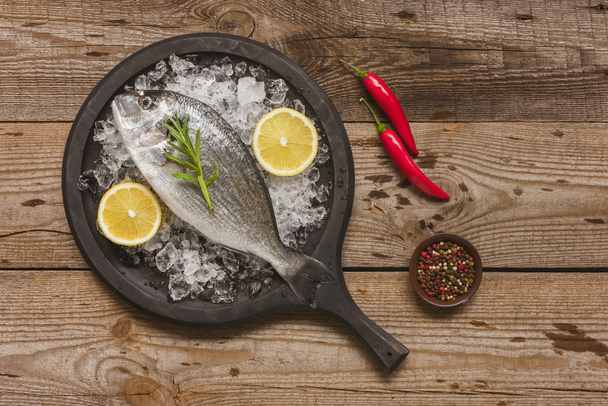 верхний вид подноса с сырой рыбой, розмарином и лимоном на столе
 - Фото, изображение