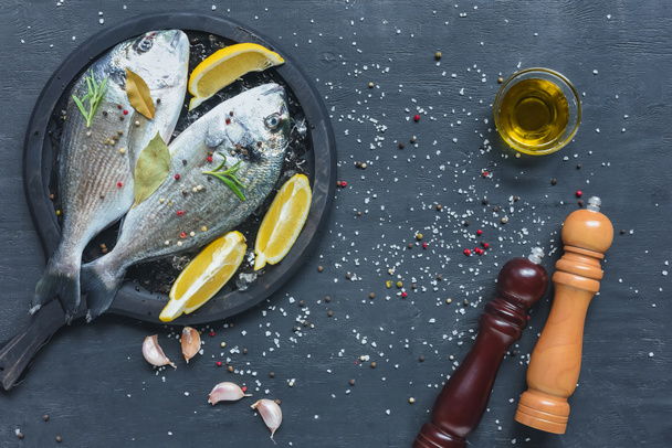 Nahrungsmittelzusammensetzung mit rohem Fisch in Tablett auf schwarzem Tisch mit Zutaten - Foto, Bild