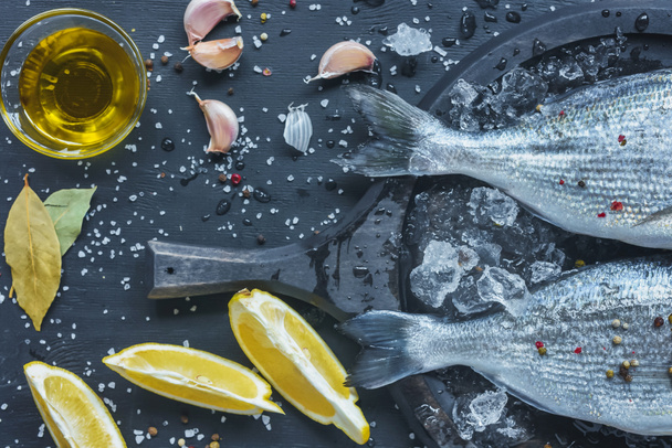 vista desde arriba de aceite de oliva, limón y ajo cerca de bandeja con pescado crudo
 - Foto, Imagen
