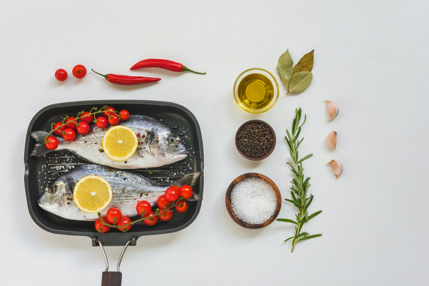 elevated view of ingredients, uncooked fish decorated by lemon and cherry tomatoes in baking tray on white table  - 写真・画像