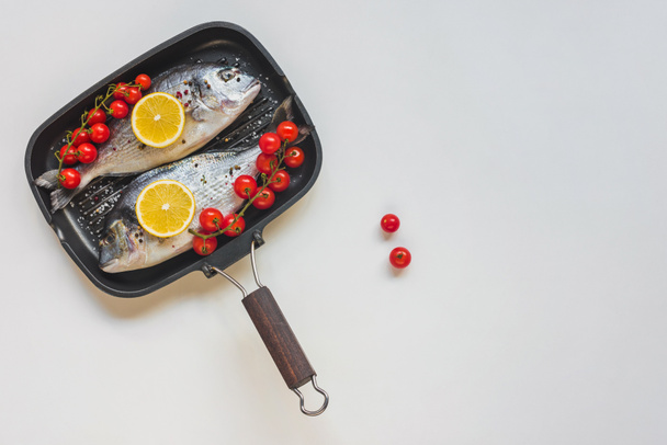вид на сырую рыбу, украшенную помидорами лимона и черри в подносе для выпечки
 - Фото, изображение