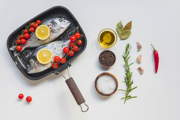 view from above various ingredients, uncooked fish decorated by lemon and cherry tomatoes in baking tray - Photo, Image