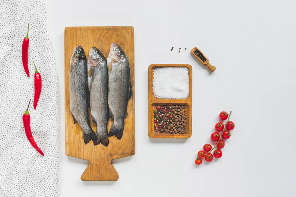 top view of uncooked fish on wooden board near ingredients on white table  - Foto, afbeelding
