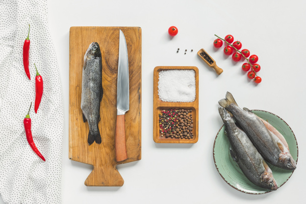 elevated view of uncooked fish on wooden board near ingredients on white table  - Foto, imagen